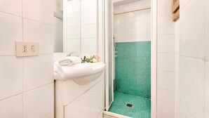 Une salle de bain avec des carreaux blancs, un lavabo avec une serviette, et une douche avec des carreaux verts.