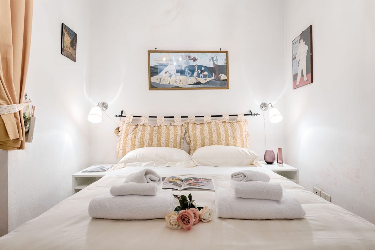 A neatly made bed with towels, a bedside table with a book, and a wall-mounted lamp.