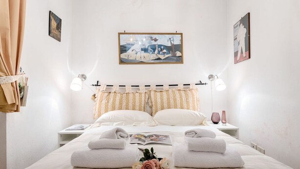 Un lit bien fait, avec des serviettes à portée de main, une table de chevet sur laquelle repose un livre et une lampe fixée au mur.