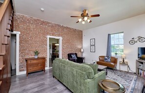 A living room with a brick wall, a ceiling fan, a green sofa, a wooden sideboard, and a dining area.