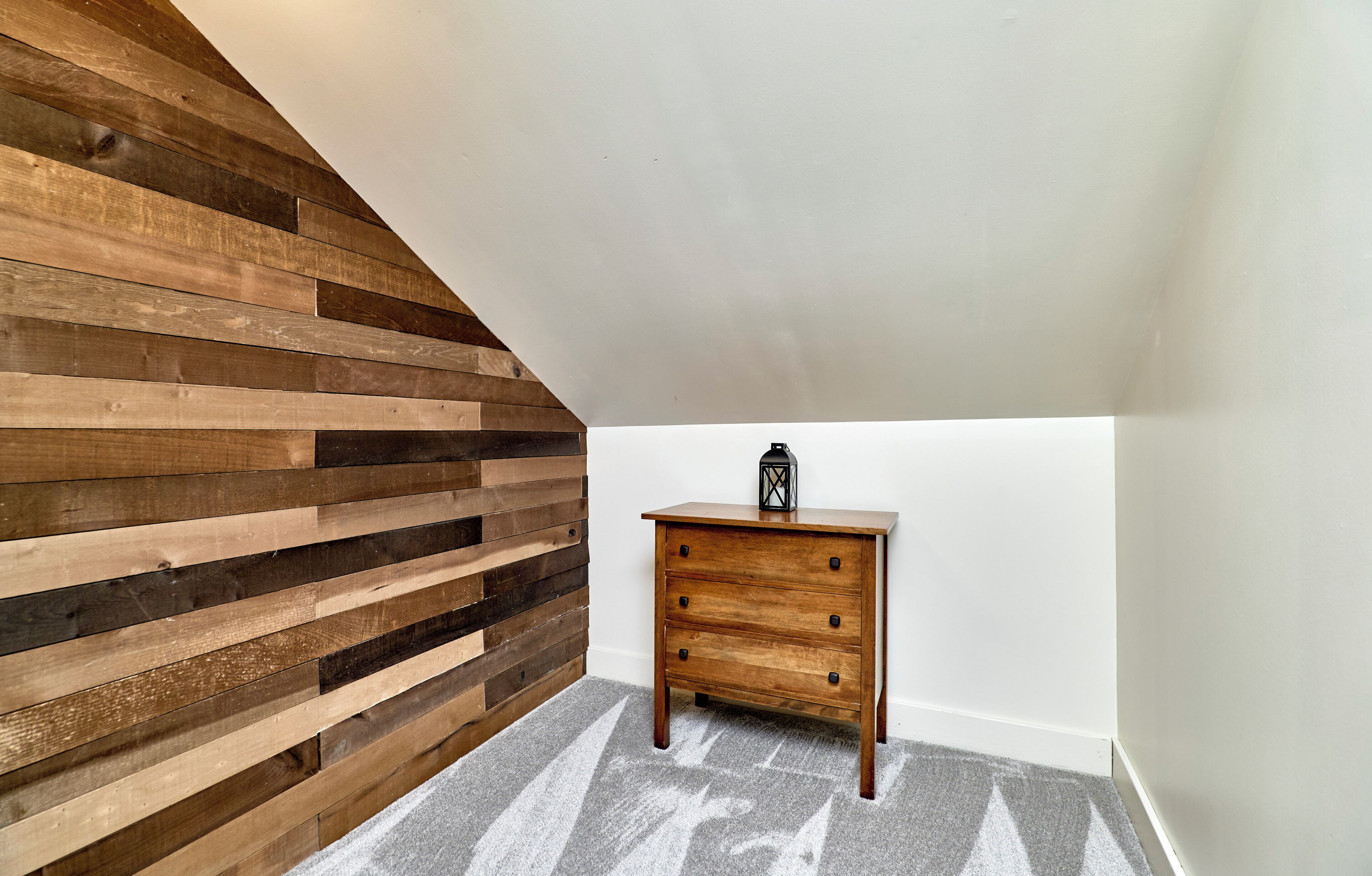 A room with a sloped ceiling, a wooden wall, and a small wooden dresser with drawers.