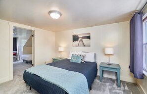 A bedroom with a bed, two bedside tables, a nightstand, a lamp, a painting, and a window with curtains.
