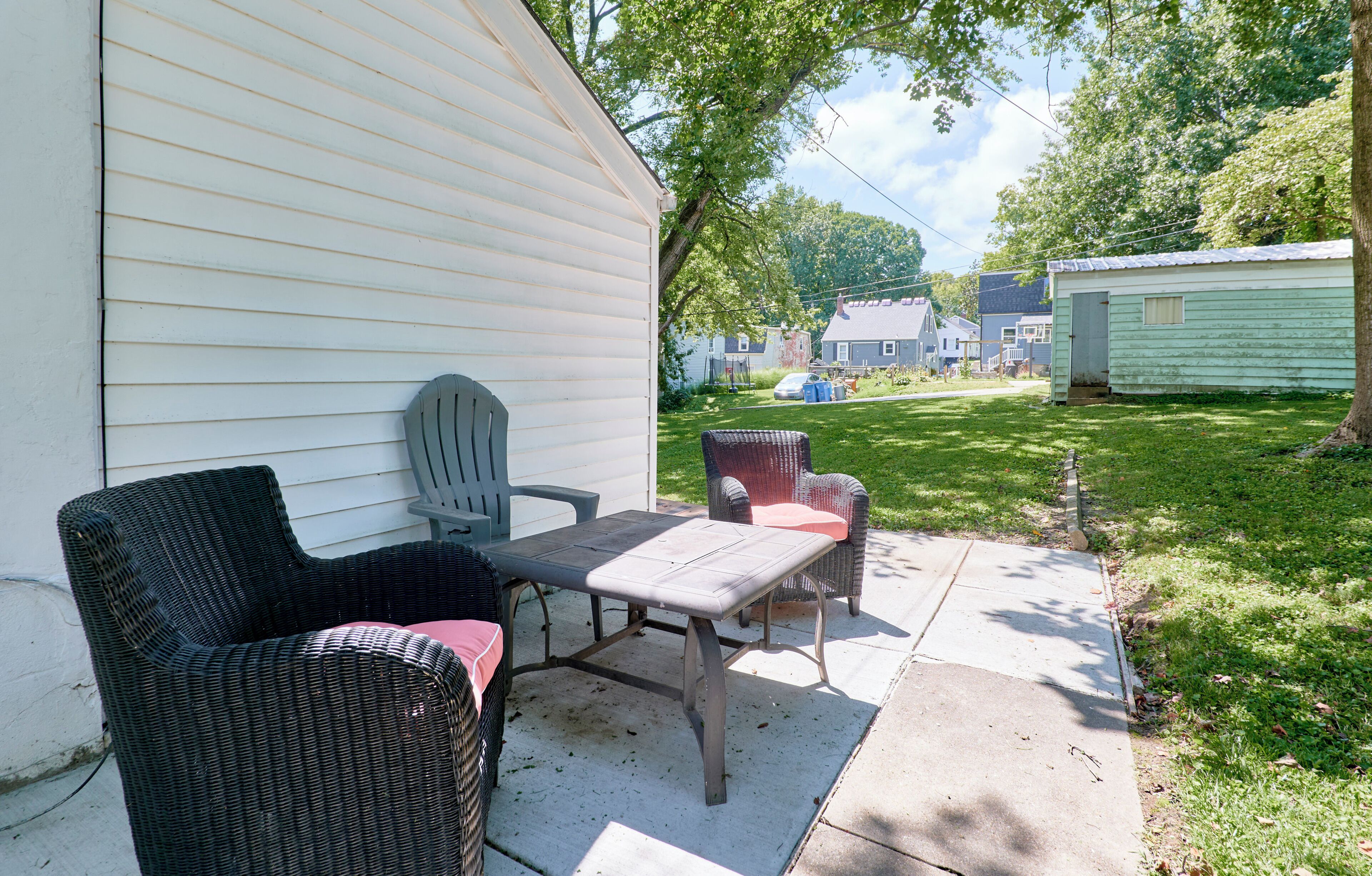 A patio with wicker furniture and a concrete table, adjacent to a white house with a visible garage.