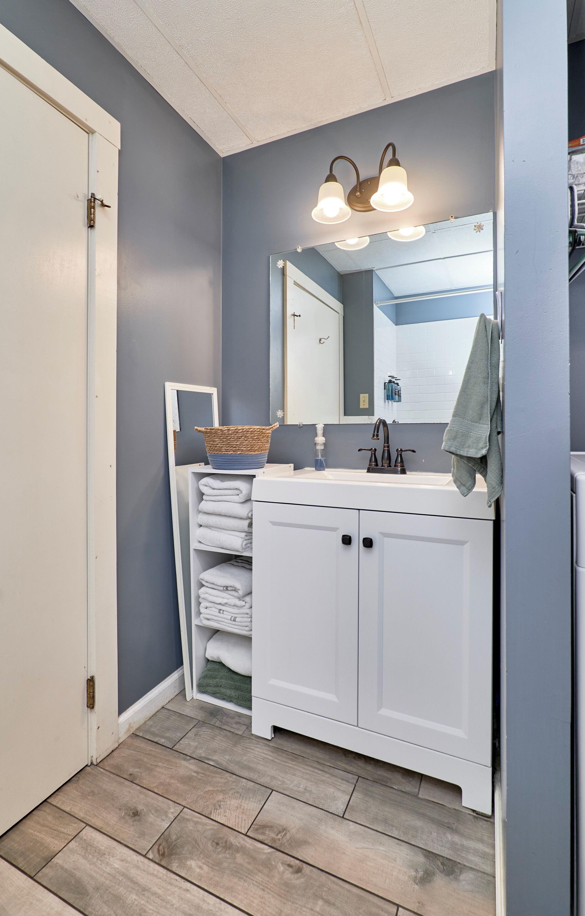 Une salle de bain avec un meuble-lavabo blanc, un miroir, un luminaire et un plancher en bois.