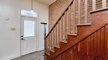 A staircase with wooden steps and a metal railing, leading to a room with a white door and a light fixture above it.