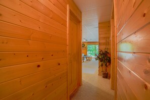 Ein Holzboden-Flur mit einer Tür zu einem Zimmer, das ein großes Fenster und eine Pflanze hat.