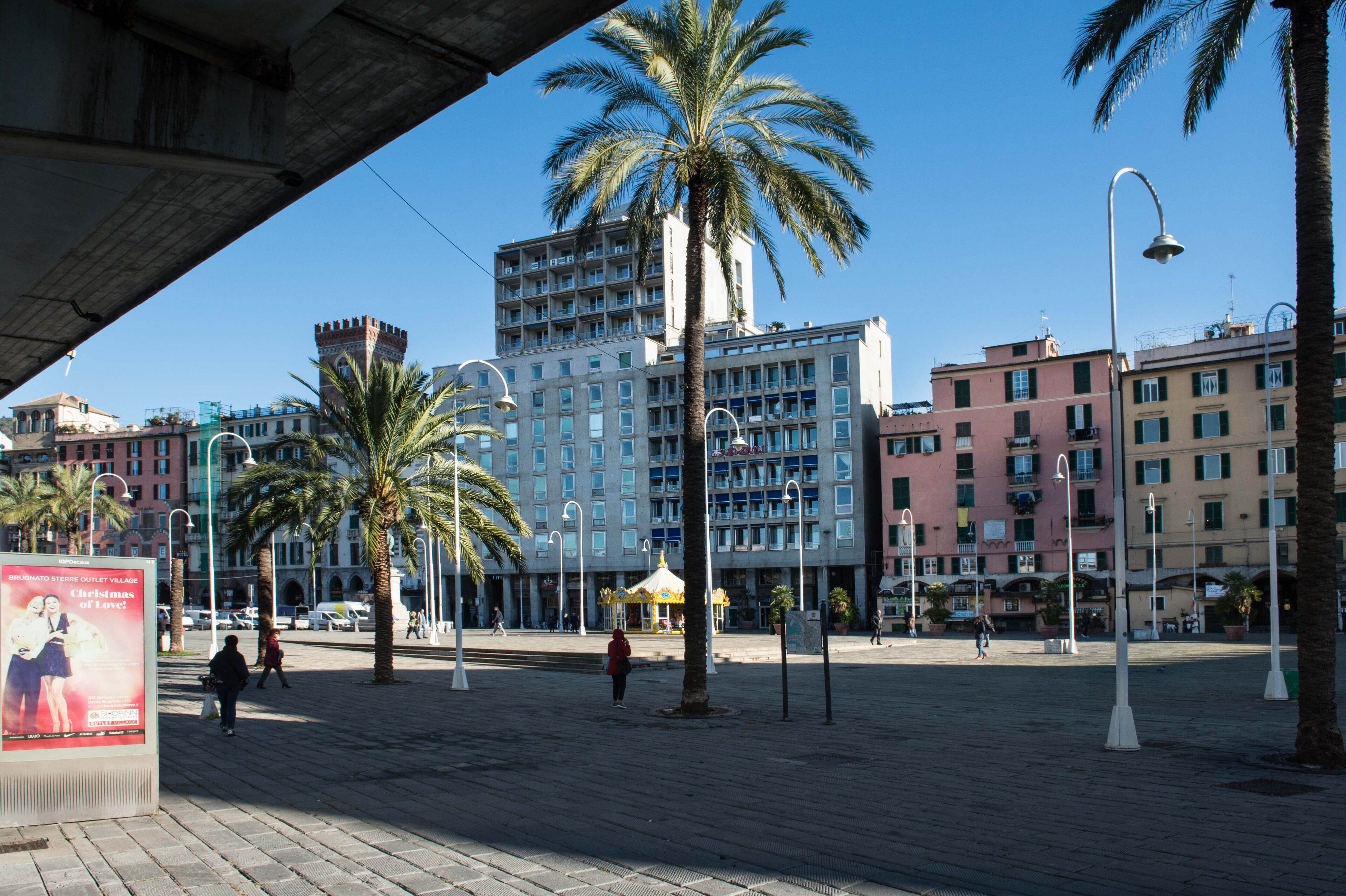 Une place publique bordée de palmiers, avec un kiosque et des bâtiments en arrière-plan.