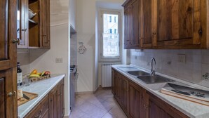 A kitchen with wooden cabinets, a white countertop, a window, and a radiator. - Pontormo, a cozy apartment near Ponte Vecchio by Mmega (Florence)