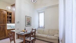 A dining area with a wooden table and chairs, a beige sofa, and a window with curtains. - Pontormo, a cozy apartment near Ponte Vecchio by Mmega (Florence)