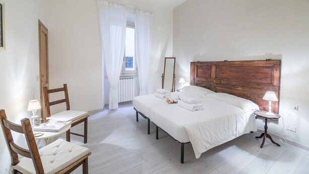A bedroom with a bed, bedside tables, a chair, a window with curtains, and a wooden headboard. - Pontormo, a cozy apartment near Ponte Vecchio by Mmega (Florence)