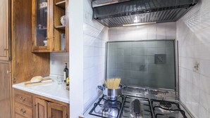 A kitchen with wooden cabinets, a gas stove, and a pot of spaghetti. - Pontormo, a cozy apartment near Ponte Vecchio by Mmega (Florence)
