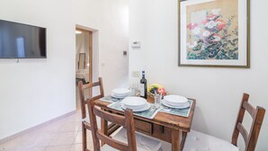 A dining area with a wooden table set for four, a framed artwork on the wall, and a television mounted above the table. - Pontormo, a cozy apartment near Ponte Vecchio by Mmega (Florence)