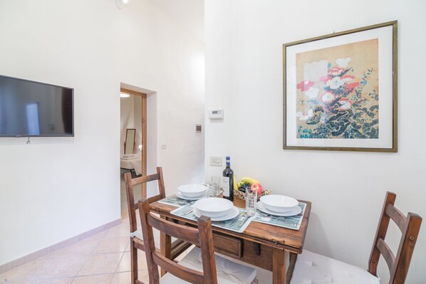 A dining area with a wooden table set for four, a framed artwork on the wall, and a television mounted above the table.