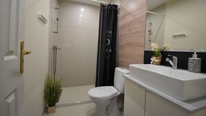 Une salle de bain moderne avec des toilettes blanches, une douche avec un rideau noir, un lavabo avec un miroir et une plante en pot.