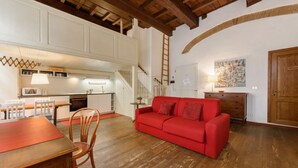 Un vaste espace de vie avec un canapé rouge, un plancher en bois, une table à manger avec des chaises, une cuisine à l’arrière-plan et un escalier.