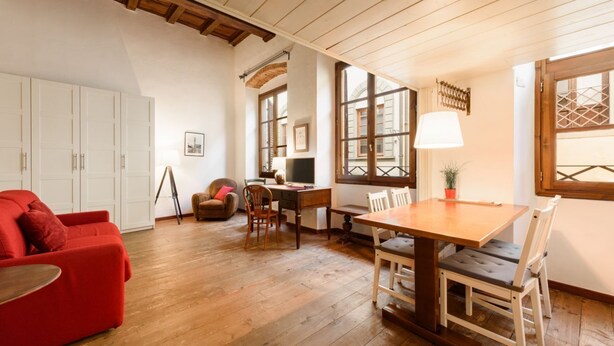 Une pièce avec une table en bois, des chaises, un canapé rouge, un bureau et une fenêtre donnant sur un beau paysage.