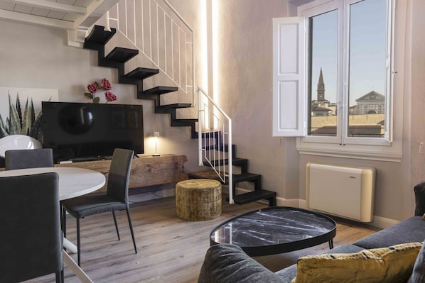 Un salon moderne avec un escalier, un coin repas et une vue sur un immeuble par la fenêtre.