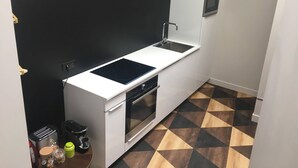 Ett kompakt kök med en vit bänkskiva, en inbyggd ugn, en mikrovågsugn och ett diskho. Golvet har ett geometriskt mönstrat kakel.
