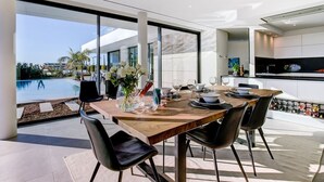 Un espace repas moderne avec une table en bois, des chaises noires et une vue sur une piscine.