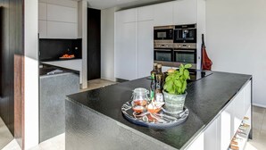 Une cuisine moderne avec des meubles blancs, un îlot central sur lequel est posé un plateau contenant divers condiments, et une plante en pot.