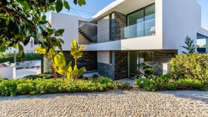 Une maison moderne à deux étages, dotée d’une façade en pierre, de grandes fenêtres et d’une allée pavée.