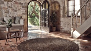 Ein Zimmer mit Steinwänden, einer Couch, einem runden Teppich und einer Treppe.