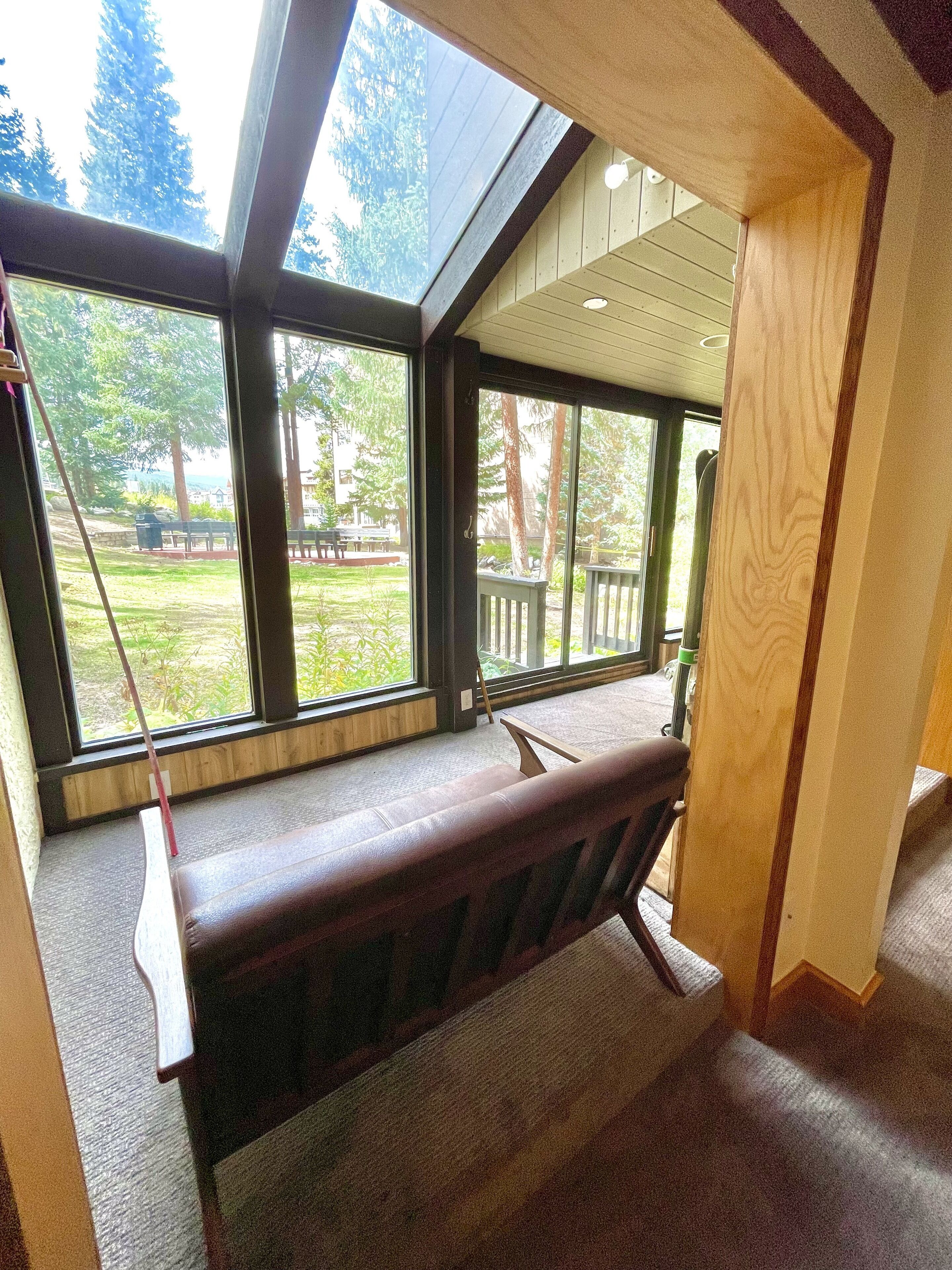 A room with a large window, a bench, and a view of a garden and trees.