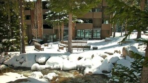 A snow-covered outdoor area with a small stream, benches, and a building in the background. - Best Ski-in/Ski-Out Condo at Copper Mountain - Sleeps 8! (Copper Mountain)