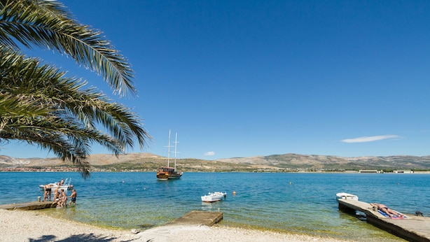 A beach with boats, clear water, and a mountainous backdrop.