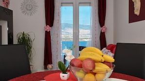 A dining table with a fruit bowl, a potted plant, and a view of the sea through a window.