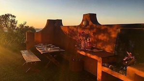 Une terrasse extérieure avec un barbecue, une table dressée pour le repas et un banc.