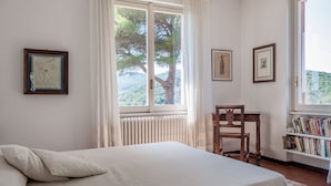 Une chambre à coucher avec un lit, une fenêtre avec des rideaux, une chaise en bois et une bibliothèque.