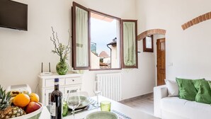 A dining area with a table set for two, a bowl of fruit, a bottle of wine, and a vase with branches. - Apartment Dreamy Guelfa by Mmega (Firenze)