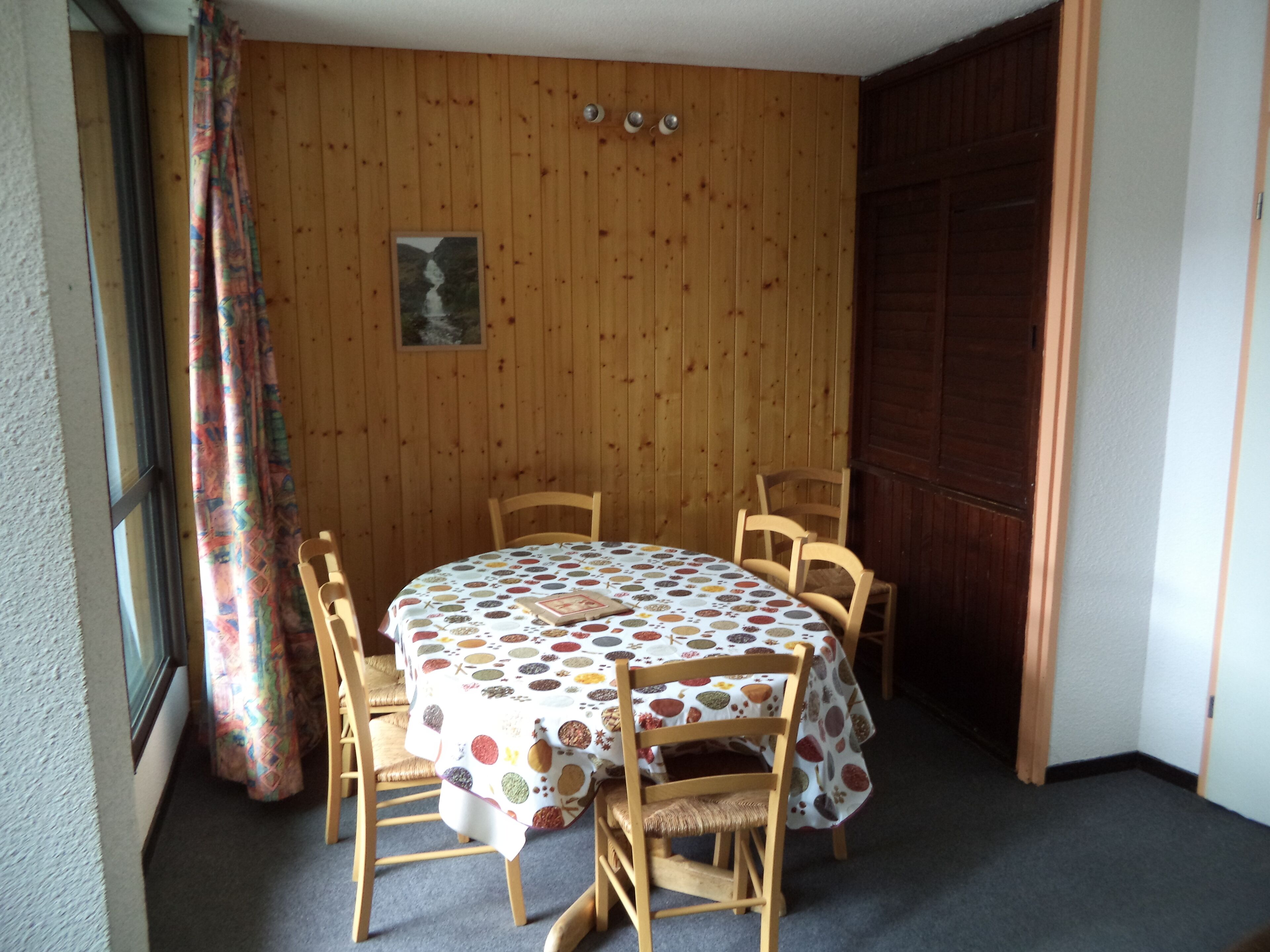 Un coin repas avec une table ronde recouverte d’une nappe à motifs, entourée de chaises en bois.