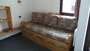 A wooden sofa with patterned cushions, a small wooden shelf with a bowl, and a framed picture on the wall. - apartments - 2 rooms - 5/6 persons (Les Belleville)