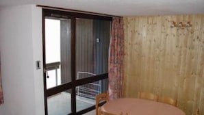 A room with a round table and four chairs, a sliding glass door, and a wooden wall with a curtain. - apartments - 2 rooms - 5/6 persons (Les Belleville)
