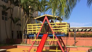A playground with a red slide and yellow and blue structures. - Beach apartment in Enseada, in a gated community, with garden and balcony. (Guaruja)