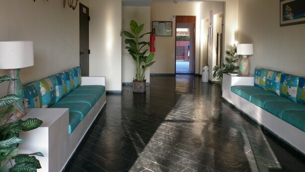 A hotel lobby with two teal sofas, a potted plant, and a ceiling light. - Beach apartment in Enseada, in a gated community, with garden and balcony. (Guaruja)