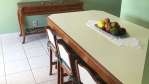 A dining area with a table set for four, a vase with flowers, and a painting on the wall. - Beach apartment in Enseada, in a gated community, with garden and balcony. (Guaruja)