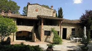 Un edificio de piedra con un patio, que presenta una escalera que lleva a una entrada cubierta, asientos al aire libre y una planta grande en maceta.
