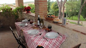 Una mesa de comedor al aire libre con platos, copas de vino y una cesta de pan.