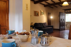 Una mesa con cafeteras, tazas y pasteles, en una habitación con vigas de madera y un sofá al fondo.
