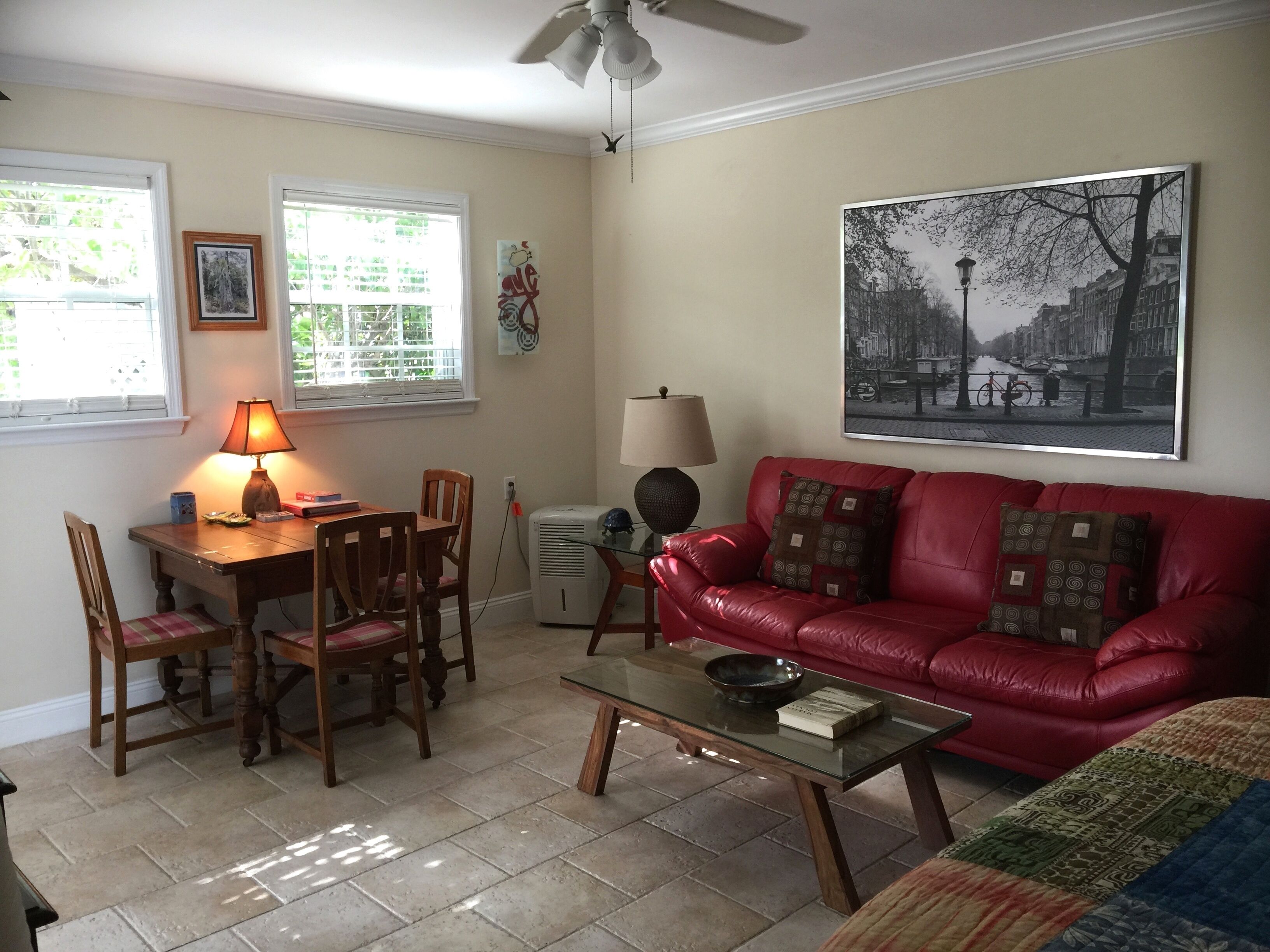 A living room with a red leather sofa, a glass coffee table, a wooden dining table with chairs, and a ceiling fan.