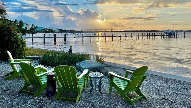 A waterfront patio with green Adirondack chairs, a small round table, and a statue. - Roonie's Periwinkle Cottage -  waterfront- 2 bikes - downtown Stuart (Stuart)