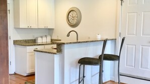 A kitchen with white cabinets, a granite countertop, a sink, and two bar stools. - Charming Beach Cottage Only 100 yds from the beach (Virginia Beach)