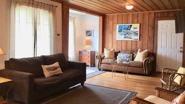 A cozy living room with a dark brown sofa, a smaller sofa with patterned cushions, a wicker chair, and a wooden coffee table. - Charming Beach Cottage Only 100 yds from the beach (Virginia Beach)