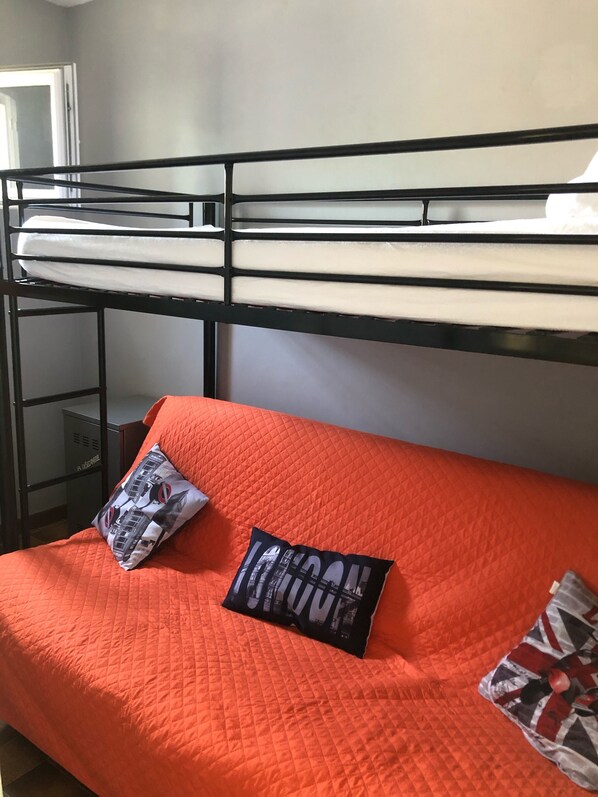 A bunk bed with a red quilted mattress and two pillows, one with a London-themed design. - Beautiful house with a garden and terrace, 400 meters from Valras and the beach. Air conditioning and Wi-Fi. (Vendres plage)