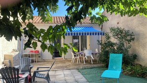 Un espace patio aménagé avec du mobilier d’extérieur, une table couverte et un fauteuil de jardin bleu.