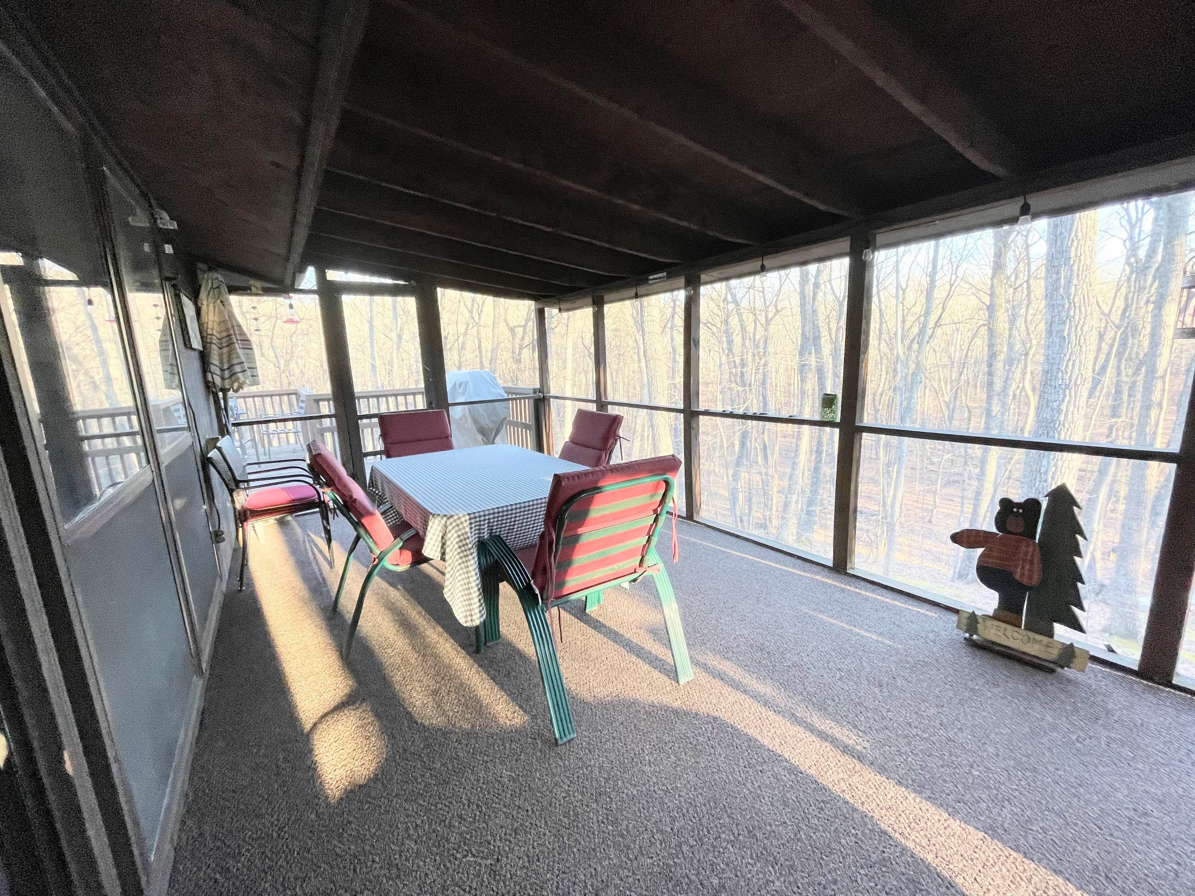 A covered outdoor seating area with a table and chairs, large windows, and a welcome sign.