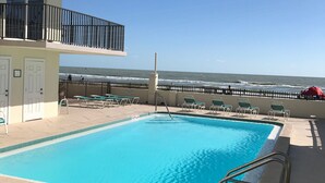 A swimming pool with a view of the ocean, surrounded by lounge chairs and a building with balconies.